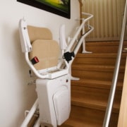 Lehner Alpha Zusammengeklappter Treppenlift mit beigem Sitzpolster an einer Holztreppe im Innenbereich.