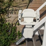 Außen-Treppenlift mit weißem Sitz an einer Holztreppe im Gartenbereich installiert.
