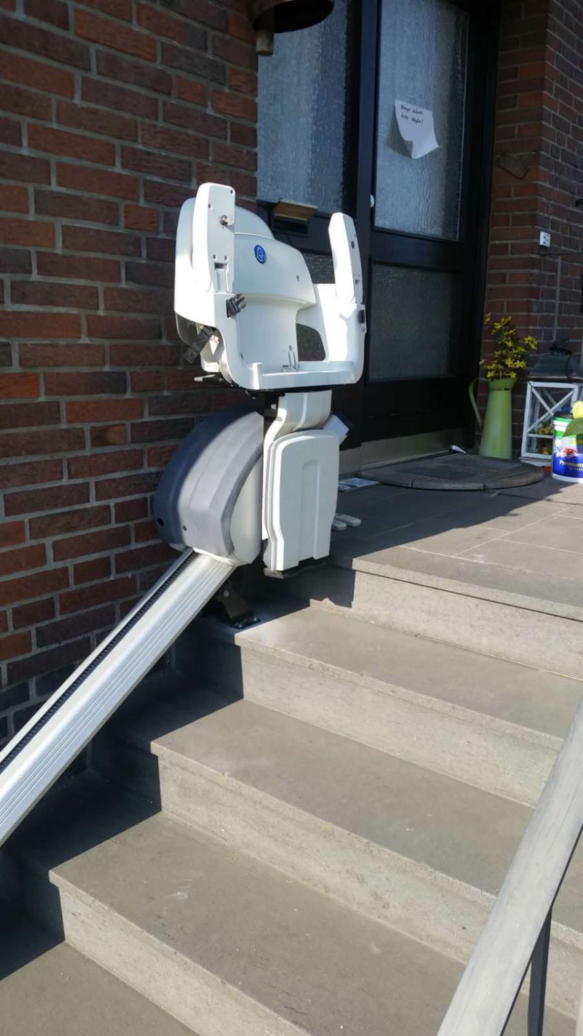 Außen-Treppenlift an einer kurzen Steintreppe vor dem Eingang eines Hauses montiert.