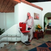 Lift Raumansicht Frau steht neben einem roten Treppenlift in einem wohnlich eingerichteten Hausflur.