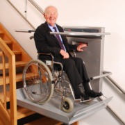 Plattformlift Älterer Mann im Rollstuhl fährt mit einem Plattformlift eine Treppe hinauf und lächelt