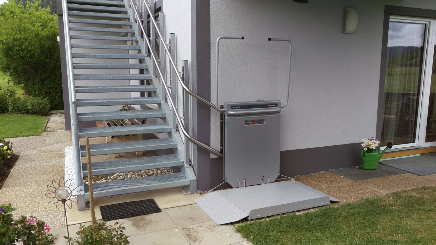 Plattformlift Plattformlift im Außenbereich an einer Metalltreppe neben einem Wohnhaus installiert.