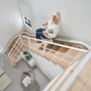Flow-X_Main-13-scaled Seniorin fährt mit einem Treppenlift eine gewendelte Holztreppe in einem modernen Wohnhaus hinab.
