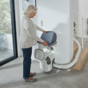 Flow-X_Main-5-scaled Seniorin klappt den Sitz eines Treppenlifts im modernen Wohnzimmer hoch.