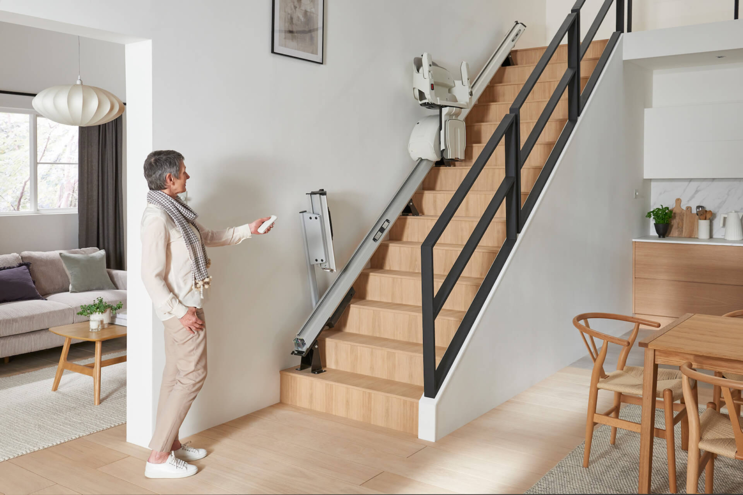 Lift zu sich rufen Ältere Frau steuert mit einer Fernbedienung einen Treppenlift an einer modernen Holztreppe im Wohnzimmer.