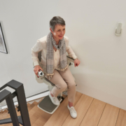 Treppenlift wird in einem modernen Haus benutzt 2 Ältere Frau fährt mit einem Treppenlift eine moderne Holztreppe hinauf.