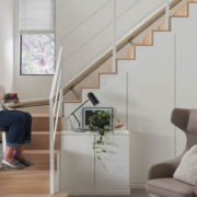 Treppenlift (kurvige Treppe) Seniorin fährt mit einem Treppenlift eine moderne Holztreppe in einem hellen Wohnzimmer hinauf.