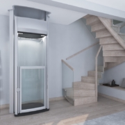 Moderner Homelift mit Glasfront neben einer Holztreppe in einem hell gestalteten Wohnbereich.