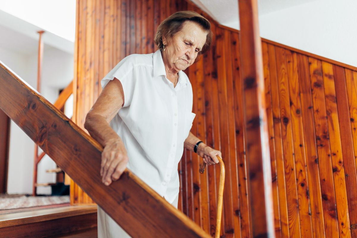 Treppe als Hindernis Seniorin geht mühsam ihre alte Holztreppe herunter, bevor diese barrierefrei umgebaut wird